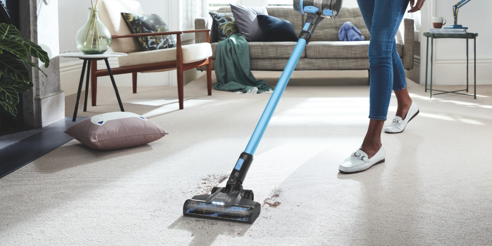 Using a lightweight cordless Vax vacuum cleaner to clean a cream carpet