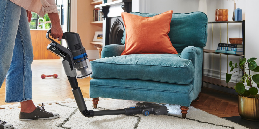 Using a Vax vacuum cleaner to clean under a teal sofa